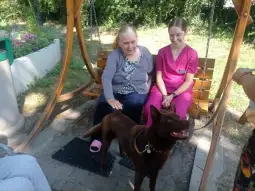 Kobieta w różowym stroju i starsza pani na huśtawce z psem obok.