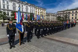 Ceremonia wojskowa z żołnierzami w mundurach i flagami na placu.