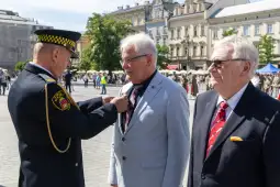 Ceremonia wręczenia odznaczeń w plenerze, mężczyźni w garniturach, mundur policyjny.