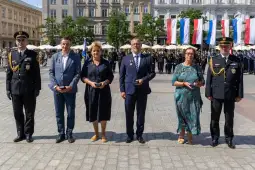 Uroczystość z medalami, pięć osób w formalnych strojach na tle flag i mundurowych.