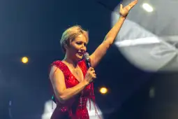 Kobieta w czerwonej, błyszczącej sukience śpiewa do mikrofonu na scenie.