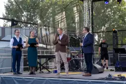 Czterech prowadzących na scenie, w tle instrumenty muzyczne i publiczność.