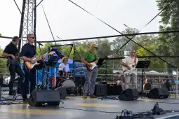 Zespół grający na scenie, instrumenty muzyczne, publiczność w tle.
