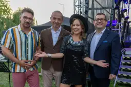 Cztery osoby w eleganckich strojach, uśmiechające się i pozujące na tle sceny.