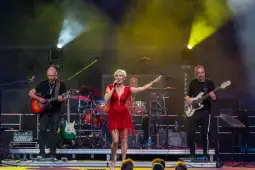 Wokalistka w czerwonej sukience występuje na scenie z zespołem muzycznym.