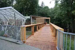 Drewniany taras prowadzący do nowoczesnego budynku w otoczeniu zieleni.