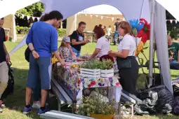 Ludzie przy stoisku z jedzeniem i roślinami podczas festiwalu na świeżym powietrzu.