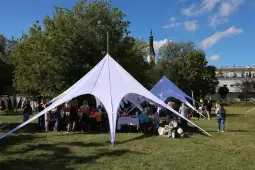 Ludzie bawią się pod białymi namiotami na zielonej przestrzeni w słoneczny dzień.
