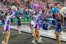 Grupa cheerleaderek w strojach sportowych wykonuje układ taneczny na hali sportowej.