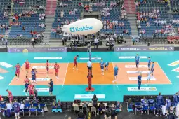 Mecz siatkówki w hali sportowej z drużynami w niebieskich i czerwonych strojach.