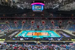 Mecz siatkówki w dużej hali sportowej z widownią wypełnioną kibicami.