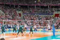 Mecz siatkówki w hali sportowej z widownią wypełnioną kibicami.