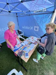 Kobieta rozmawia z pracownicą stoiska informacyjnego, obok ulotki i materiały promocyjne.