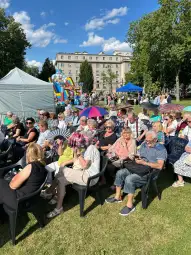 Tłum ludzi siedzących na krzesłach, w tle atrakcje festiwalowe i zielona przestrzeń.