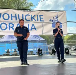 Dwie policjantki na scenie, jedna z mikrofonem, druga obok, w tle baner z napisem WOHUCKIE.