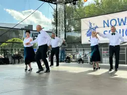 Grupa tańczących osób w eleganckich strojach na scenie podczas wydarzenia.