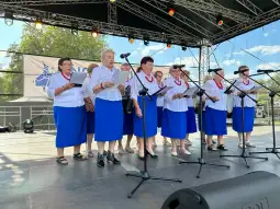 Grupa kobiet w niebieskich spódnicach śpiewa na scenie podczas występu.