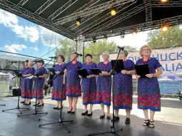 Grupa kobiet w kolorowych sukienkach śpiewa na scenie podczas występu.