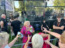 Kobieta w różowej sukience rozdaje napoje na festiwalu, w tle tłum i scena.