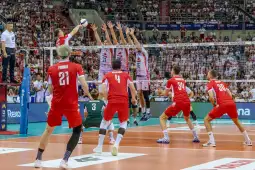 Mecz siatkówki, zawodnicy w czerwonych strojach atakują piłkę.