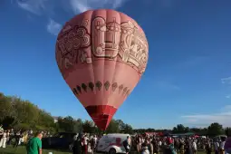 Balon na gorące powietrze w różowym kolorze z rysunkami, otoczony tłumem ludzi.