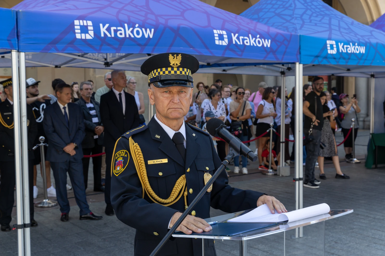 Mężczyzna w mundurze stoi przy mównicy, w tle tłum ludzi i namioty z logo Krakowa.  Autor: Bogusław Świerzowski