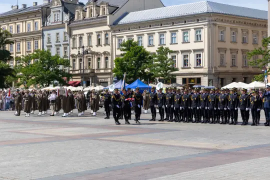 Uroczysta parada z udziałem wojskowych i orkiestry na tle zabytkowych budynków.