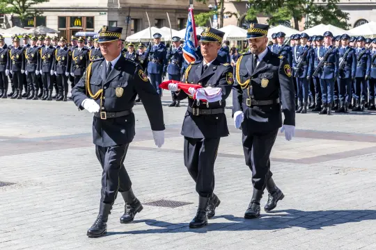 Trzech mężczyzn w mundurach niesie flagę podczas ceremonii wojskowej.
