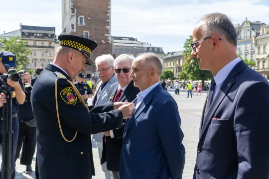 Ceremonia wręczenia odznaczenia mężczyźnie przez funkcjonariusza w mundurze.