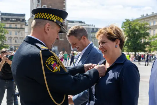 Wręczenie odznaczenia przez funkcjonariusza policji kobiecie w eleganckim stroju.