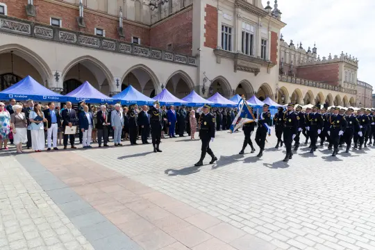 Parada z udziałem strażaków i gości na tle historycznej architektury.