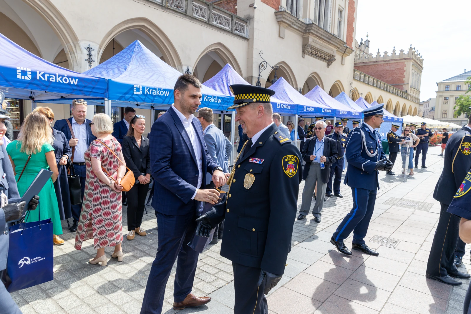 Spotkanie przedstawicieli władz i służb mundurowych w Krakowie. Stoiska informacyjne w tle.  Autor: Bogusław Świerzowski