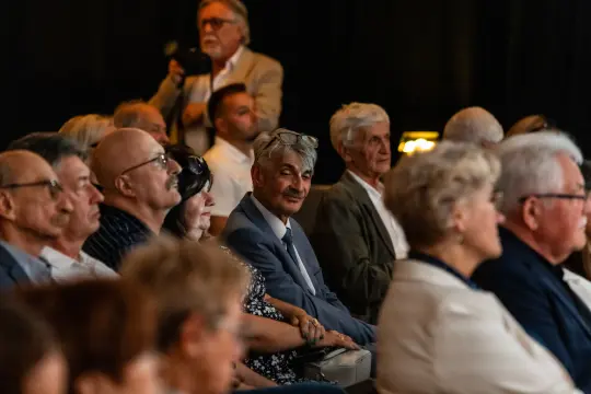 Grupa ludzi siedzących na widowni, niektórzy w okularach, w różnym wieku.