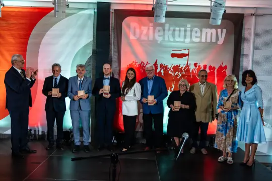 Uroczystość wręczenia nagród z udziałem ośmiu osób na scenie.