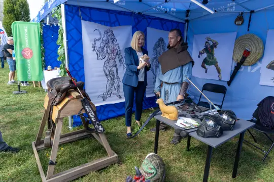 Stoisko z rekonstrukcją historyczną, postacie w strojach z epoki, akcesoria i ilustracje.
