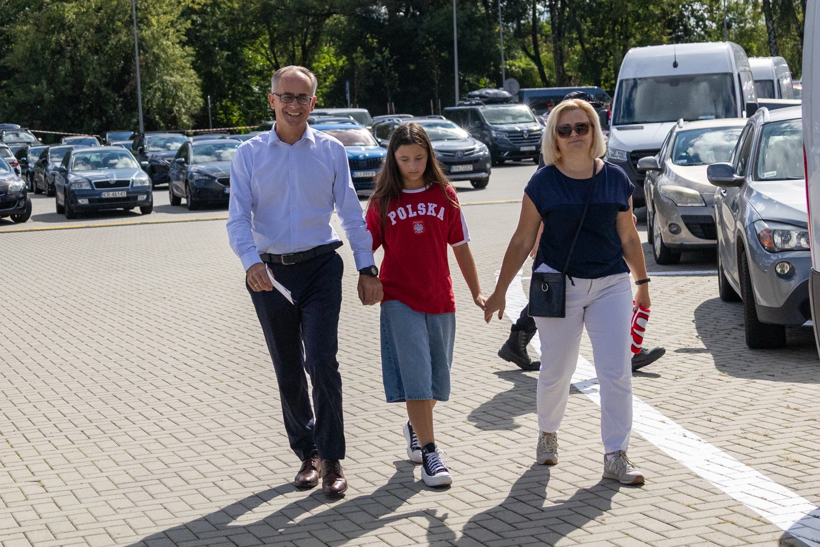 Rodzina spacerująca po parkingu, trzymająca się za ręce.  Autor: Bogusław Świerzowski