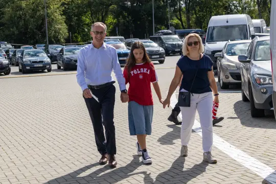 Rodzina spacerująca po parkingu, trzymająca się za ręce.