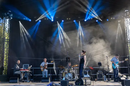 Zespół muzyczny grający na scenie, wokalistka z mikrofonem, instrumenty muzyczne.