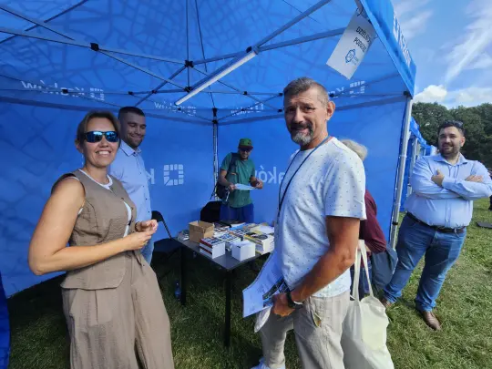 Grupa ludzi przy stoisku z materiałami promocyjnymi na wydarzeniu plenerowym.