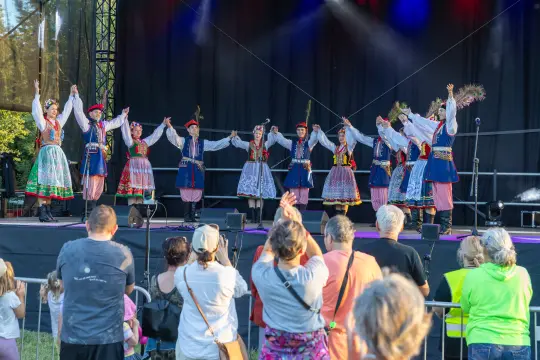 Grupa tancerzy w tradycyjnych strojach ludowych tańczy na scenie przed publicznością.