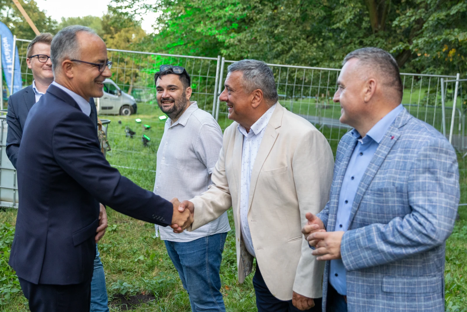 Grupa mężczyzn w formalnych strojach, uściski dłoni i rozmowy na tle zieleni.  Autor: Bogusław Świerzowski