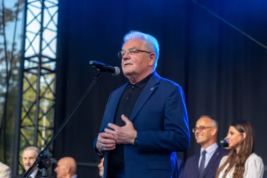Mężczyzna w garniturze przemawia do mikrofonu na scenie.