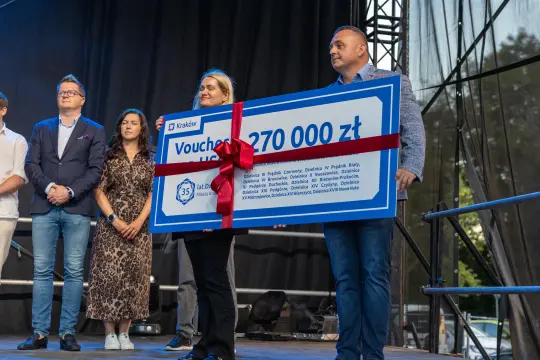 Wręczenie dużego czeku na 270 000 zł z czerwonym wstążką.