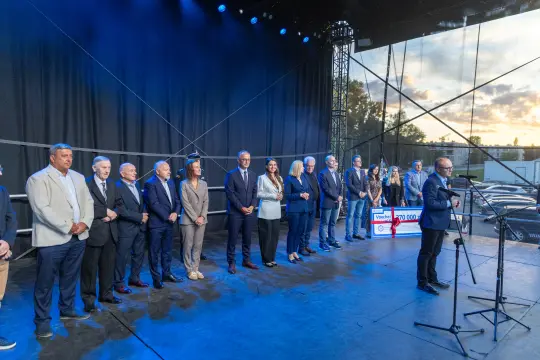 Grupa ludzi na scenie podczas wydarzenia, z mikrofonem i dużym czekiem w tle.