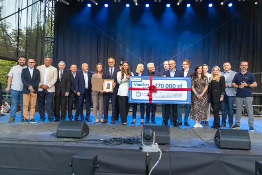 Grupa ludzi na scenie z dużym bonem na 270 000 zł, uśmiechnięci i trzymający nagrody.