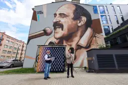 Mural z wizerunkiem mężczyzny śpiewającego do mikrofonu, obok dwóch mężczyzn przy podium.