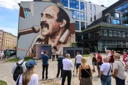 Mural przedstawiający mężczyznę z mikrofonem, otoczony przez grupę ludzi na ulicy.