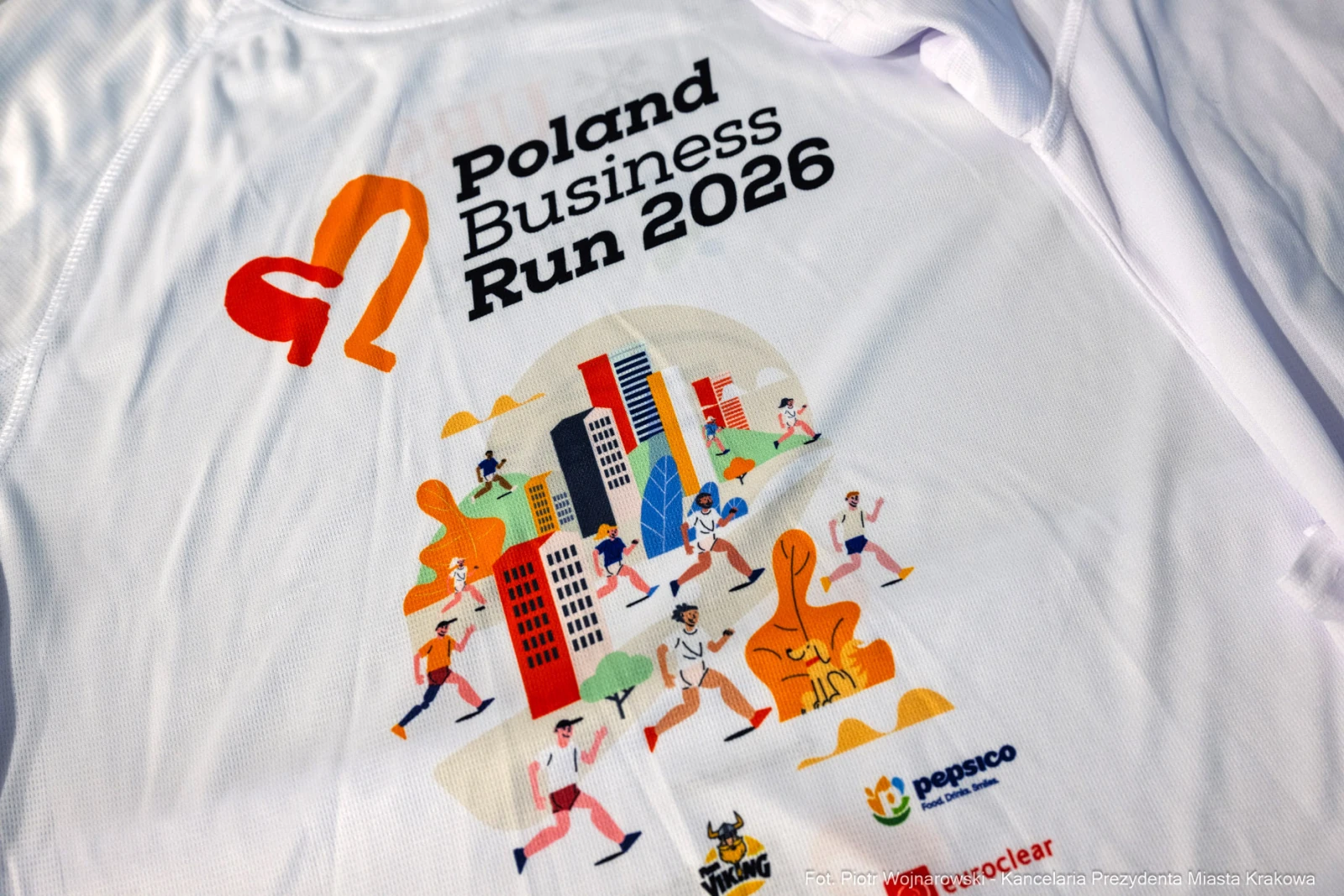 Koszulka z logo Poland Business Run 2026 i grafiką biegaczy w miejskim otoczeniu.  Autor: Piotr Wojnarowski
