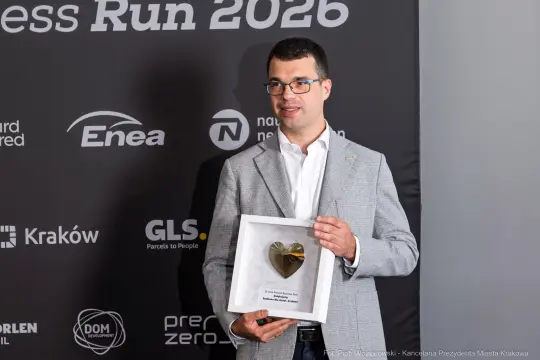 Mężczyzna trzyma nagrodę w kształcie serca na tle logo wydarzenia Business Run 2026.