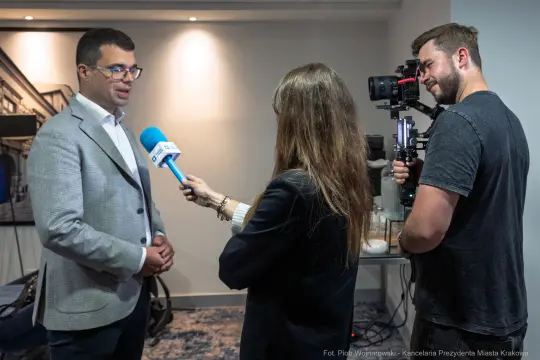 Wywiad z mężczyzną w garniturze, dziennikarka z mikrofonem, operator kamery.
